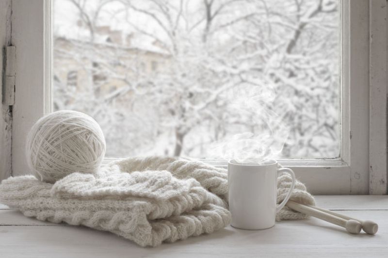 47967113 - cozy winter still life: mug of hot tea and warm woolen knitting on vintage windowsill against snow landscape from outside.